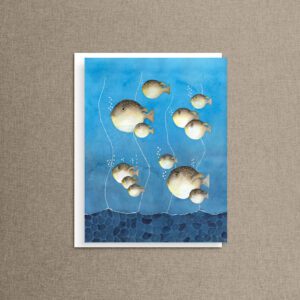 Watercolor puffer fish note card resting on a tan linen background, showing a whole family of cute pufferfish swimming together