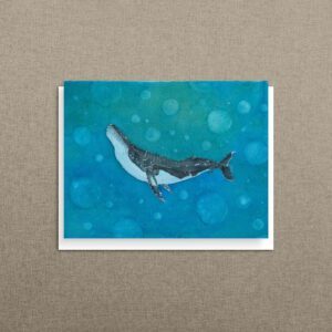 Blank humpback whale note card leaning against a natural linen background with a teal watercolor background