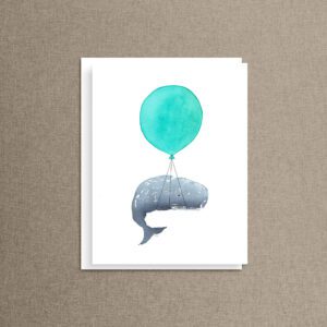Whale nursery note card with a turquoise balloon whale illustration, propped upright against a warm tan linen backdrop