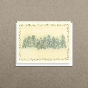 Spruced Up watercolor Christmas card of snowy evergreens aglow with twinkling lights and a swirling calligraphy border, shown with its white envelope on warm linen