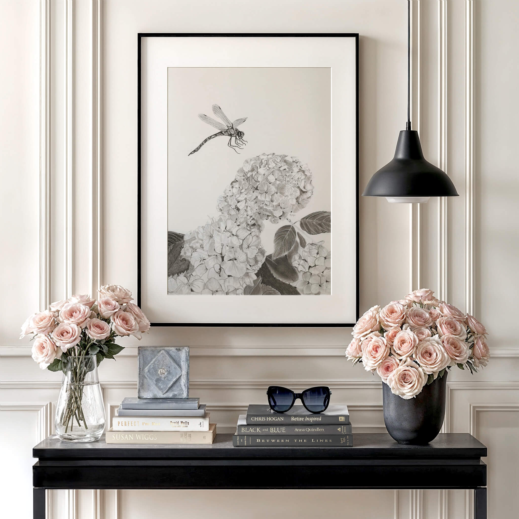Touchdown dragonfly art print in a black frame on a black console table with pink roses