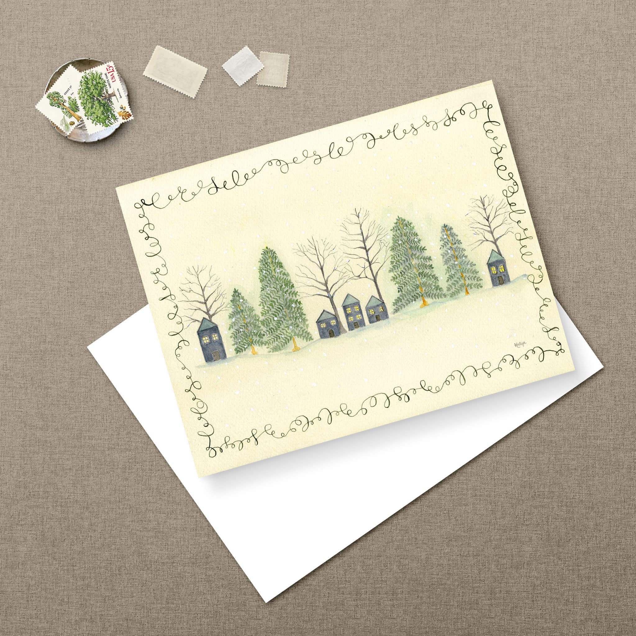 Peaceful Hilltop christmas greeting card watercolor with snowy cottages and pine trees, paired with a white envelope and vintage tree postage stamps.