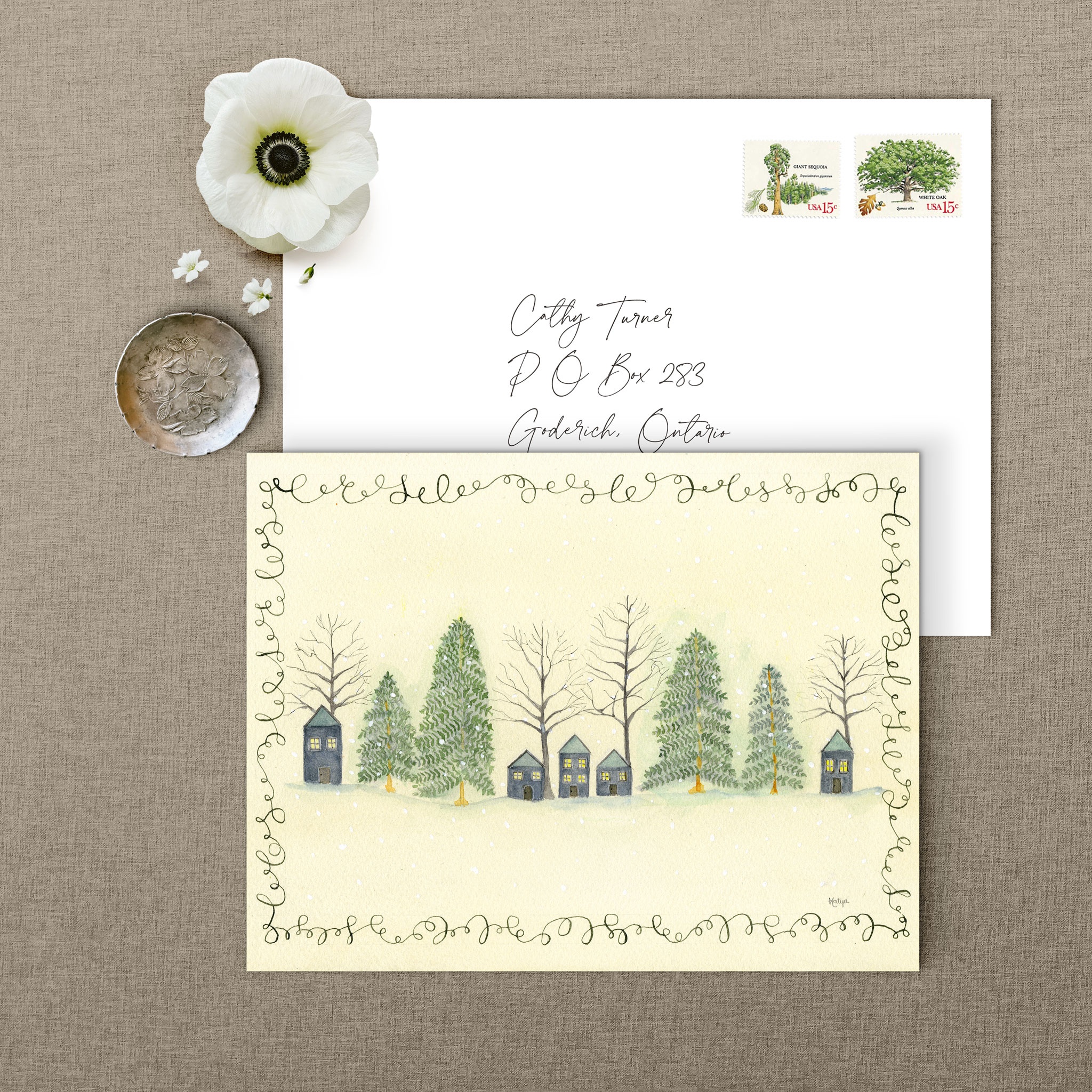 Peaceful Hilltop christmas greeting card watercolor beside a hand-addressed envelope with vintage tree stamps and a white flower