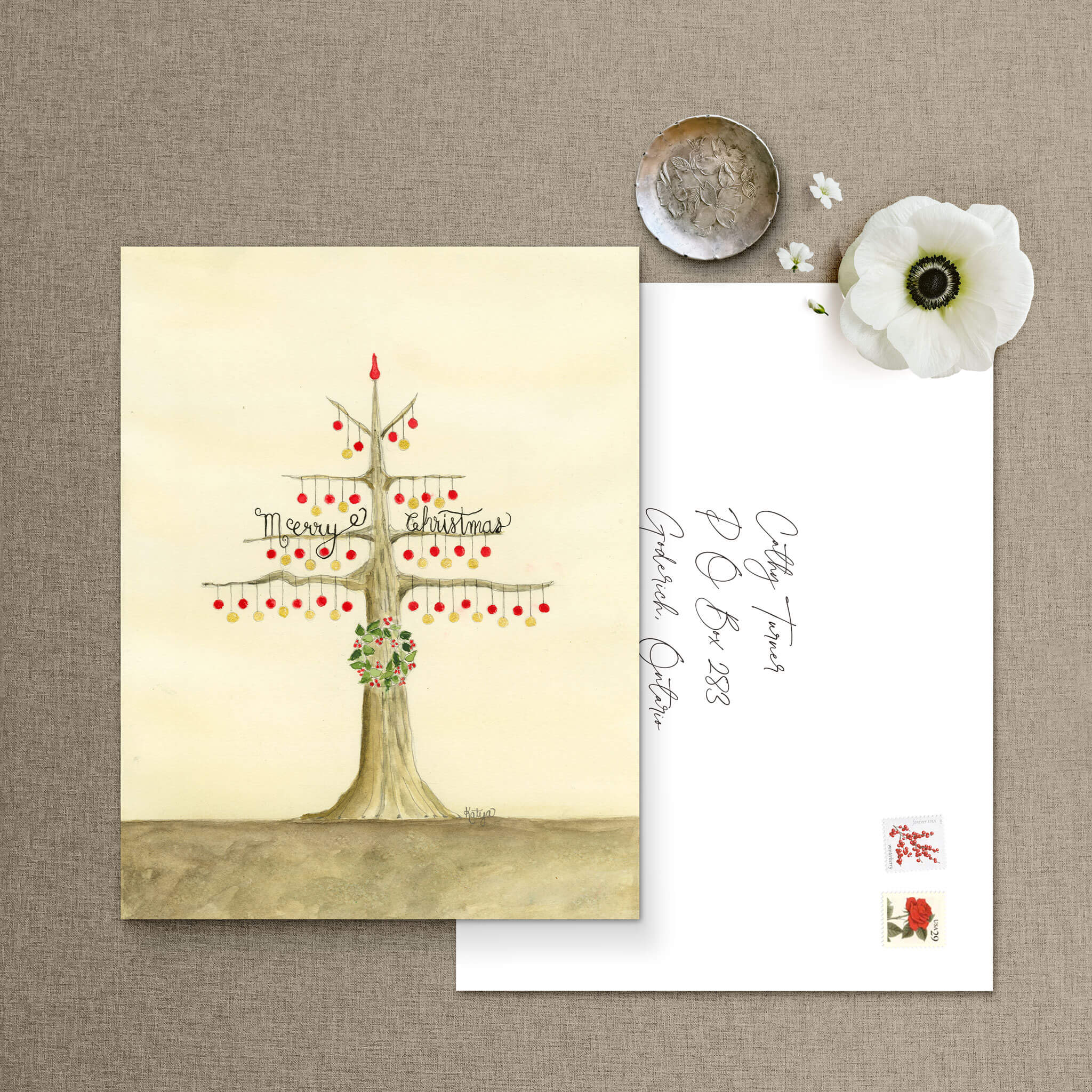 Christmas ornaments card with a watercolor bauble tree beside a hand-addressed white envelope, vintage tree stamps, and a white anemone flower.