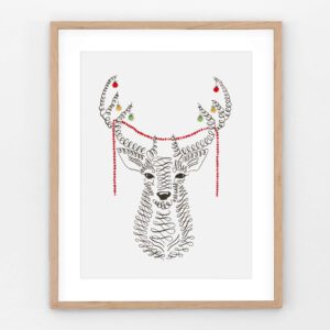 Christmas deer print of a calligraphy deer head, its antlers hung with red, green and gold baubles and a red beaded garland, in a light oak frame.