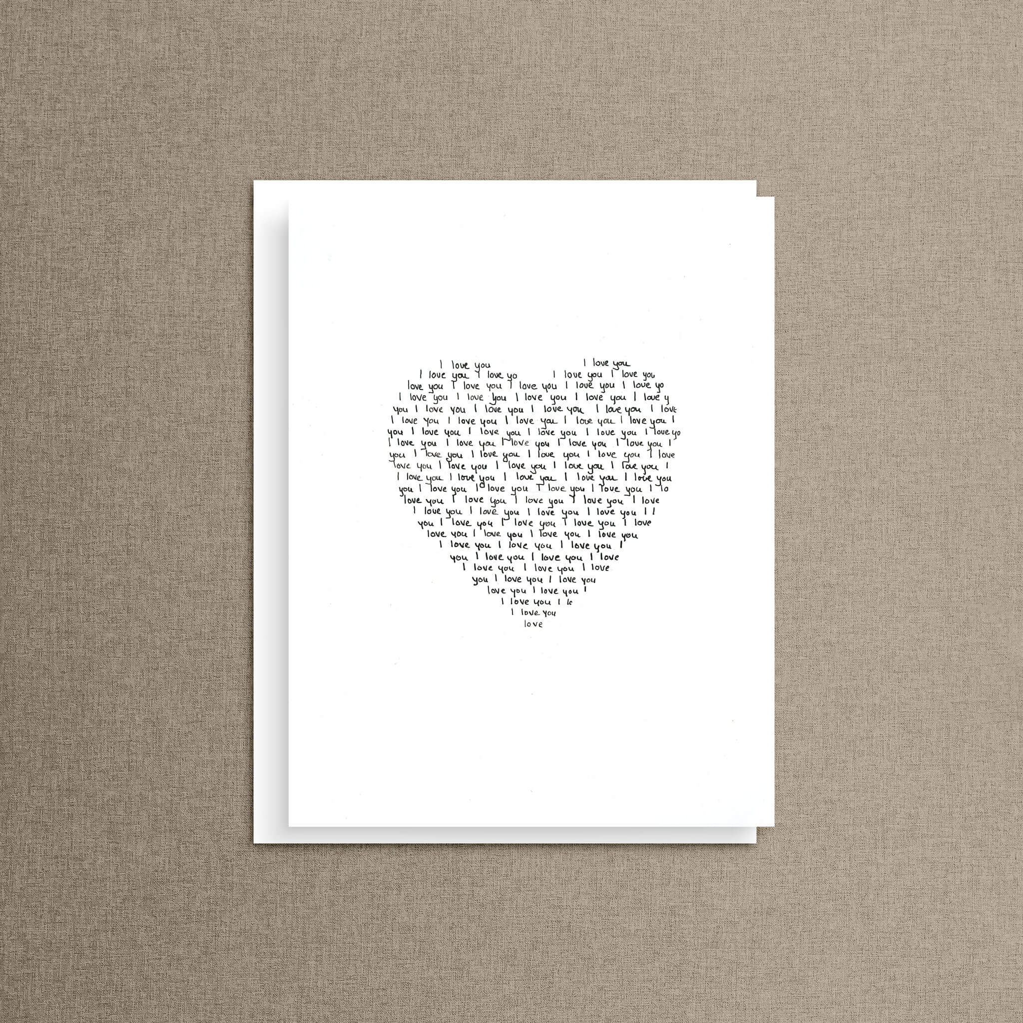 Hand-lettered heart card with "I love you" written over and over in a heart shape, displayed alone against a soft neutral linen background