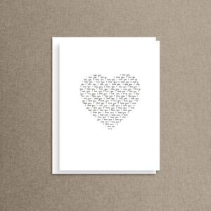 Hand-lettered heart card with "I love you" written over and over in a heart shape, standing upright on a neutral linen background