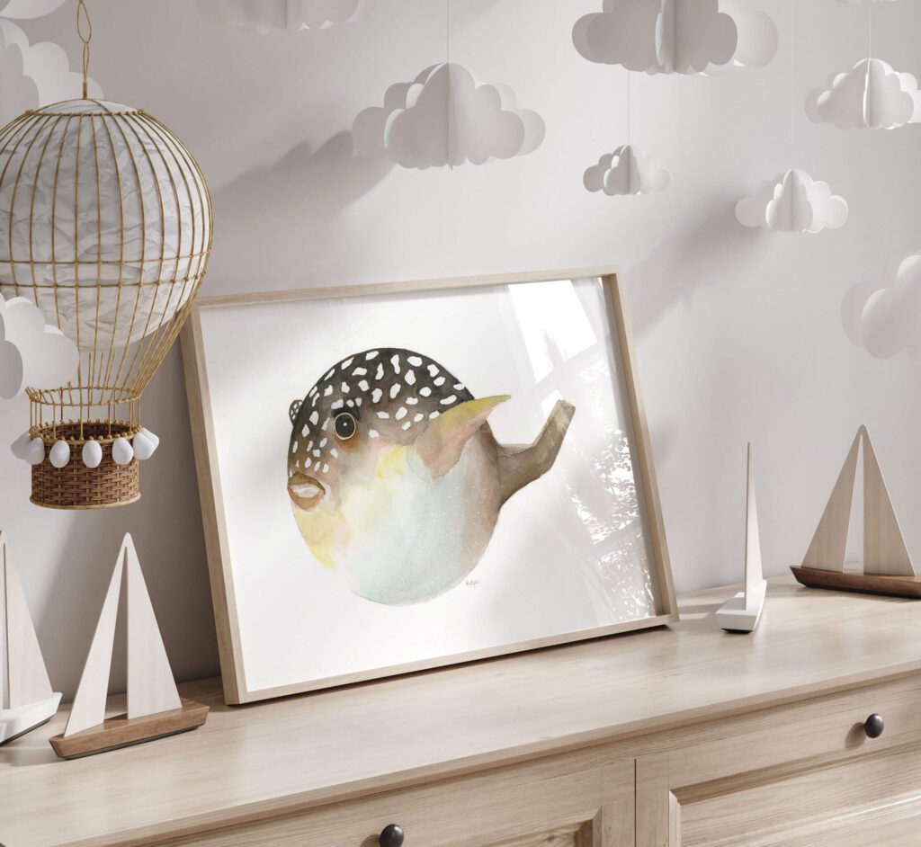 The Big Pufferfish watercolour art print of a spotted puffer fish, framed on a wooden dresser in a children’s room with paper clouds and toy sailboats, a fun gift for ocean lovers